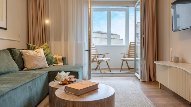 A modern living room with a green sofa, a round wooden coffee table, and a view of a balcony with outdoor seating. - Parisian-Inspired 1BR in the Heart of Bucharest - Balcony, AC & Fully Equipped (Bucharest)
