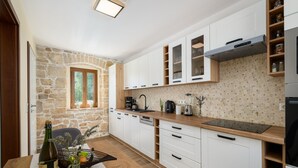 A modern kitchen with white cabinets, a stone wall, and a wooden countertop.