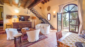 A spacious living room with a wooden staircase, a television, and a large window with a view of palm trees.