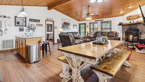 A rustic cabin interior with a wooden dining table, leather sofas, a fireplace, and various wall decorations. - Secluded Cubs Den Retreat in Wears Valley – Sleeps 10, Hot Tub, Pool Table, Dog-Friendly (Sevierville)