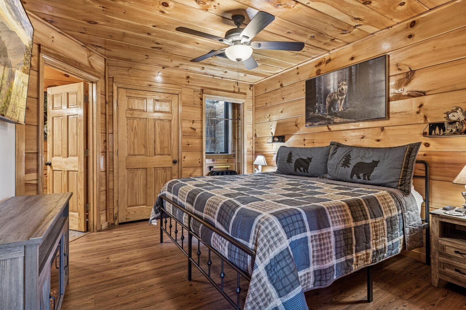 Une chambre à coucher dans une cabane en bois, avec un lit, un ventilateur de plafond et un tableau représentant un ours accroché au mur.