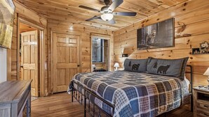 A wooden cabin bedroom with a bed, a ceiling fan, and a painting of a bear on the wall. - Secluded Cubs Den Retreat in Wears Valley – Sleeps 10, Hot Tub, Pool Table, Dog-Friendly (Sevierville)