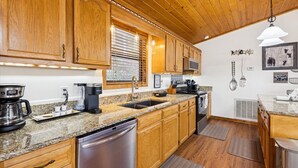 A kitchen with wooden cabinets, granite countertops, stainless steel appliances, and a window with blinds. - Secluded Cubs Den Retreat in Wears Valley – Sleeps 10, Hot Tub, Pool Table, Dog-Friendly (Sevierville)