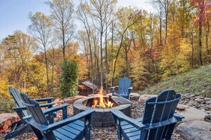 A fire pit surrounded by Adirondack chairs in a forested area.
