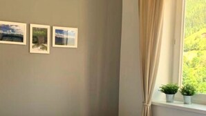 A room with a large window, a curtain, and three framed pictures on the wall. - Mountain-view Apartment in Salzburg (Bad Gastein)