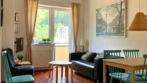 A cozy living room with a wooden floor, a sofa, a dining table with chairs, and a window with curtains. - Mountain-view Apartment in Salzburg (Bad Gastein)