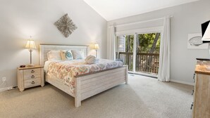 Une chambre à coucher comprenant un lit, des tables de chevet, un élément décoratif mural et une vue sur l’extérieur grâce à une porte-fenêtre coulissante.