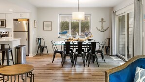 Une cuisine moderne dotée d’un îlot central, d’appareils électroménagers en acier inoxydable et d’un coin repas avec une table en verre et des chaises noires.