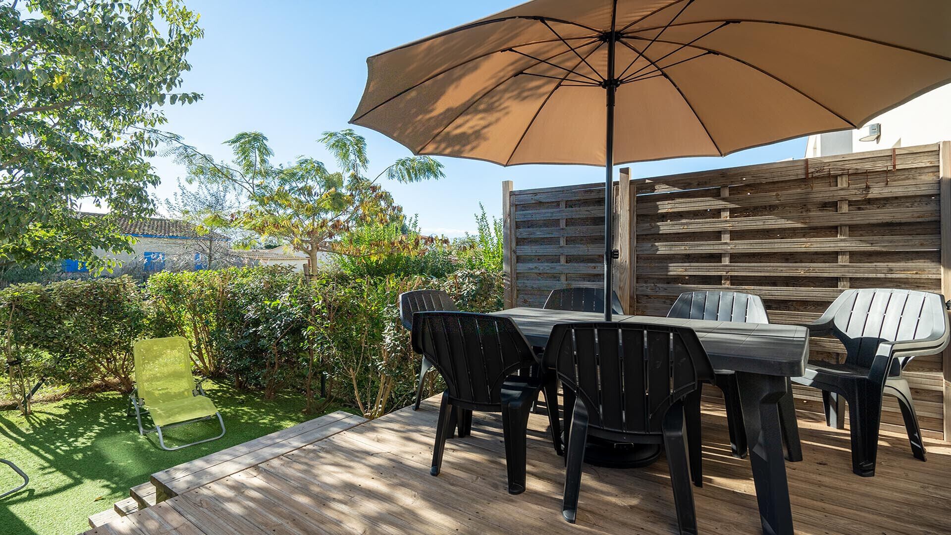 An outdoor patio with a wooden table and chairs, a large umbrella, and a wooden fence.