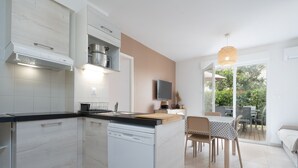 A modern kitchen with a dishwasher, a dining area with a table and chairs, and a view of the outdoors. - Sweet home duplex 6 pers (Sérignan)