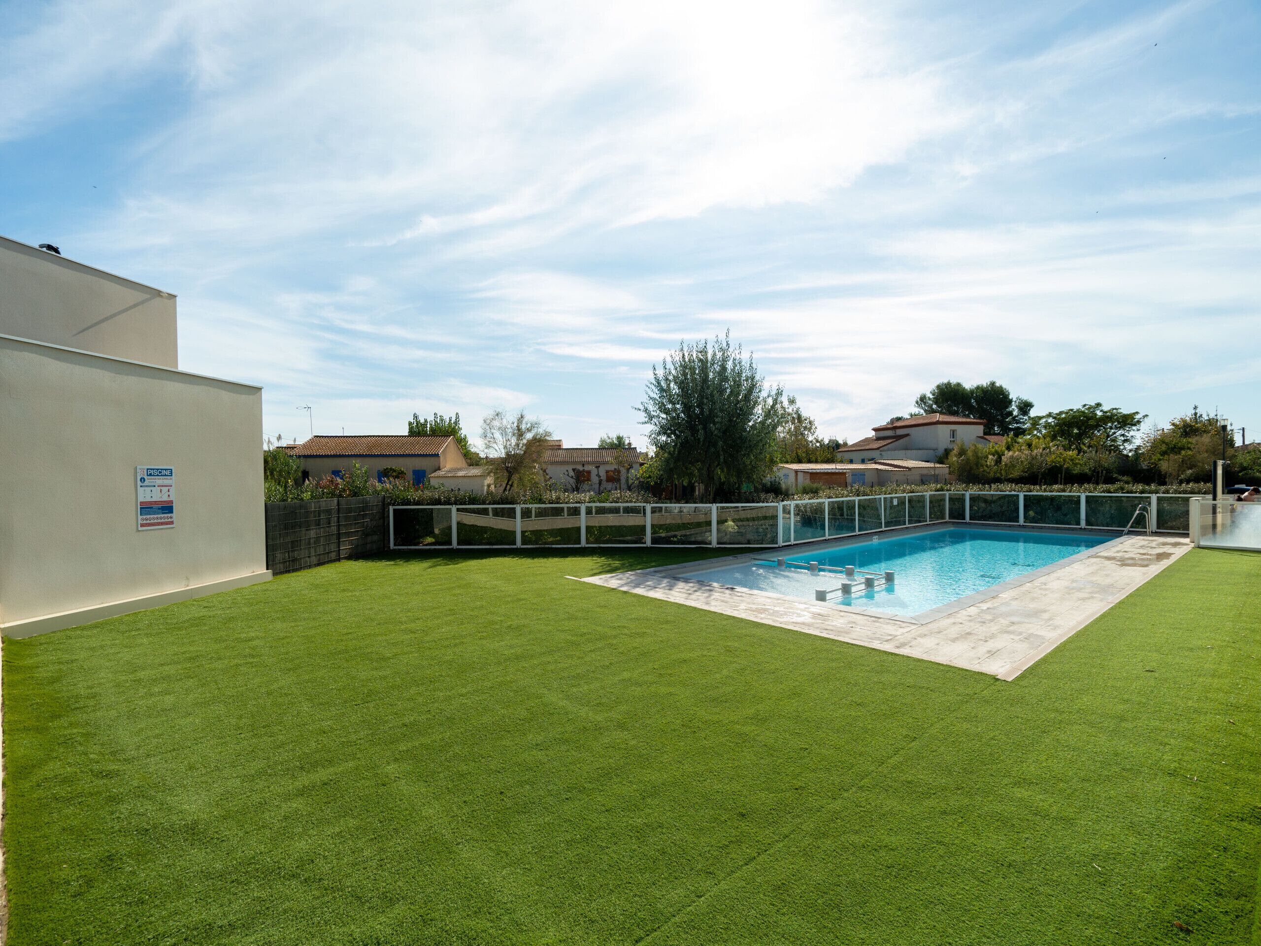 A swimming pool surrounded by a well-maintained lawn, with a fence and a sign indicating a private pool.