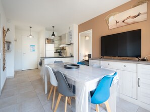 Una cucina moderna con mobili bianchi, un tavolo da pranzo con sedie, un televisore a schermo piatto e un quadro appeso al muro.