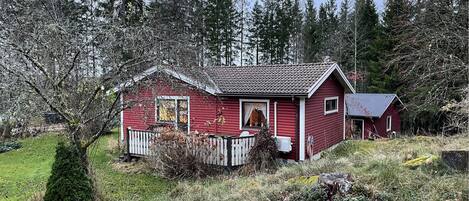 A red wooden house with a white porch, surrounded by trees and a grassy area.