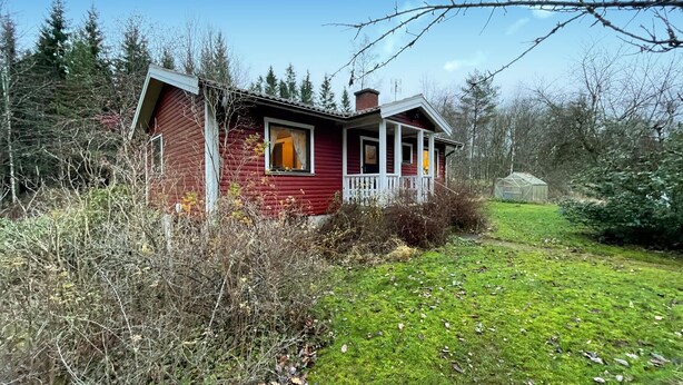 A red wooden house with a porch, surrounded by a grassy yard and dense trees. - 1 bedroom gorgeous home in Svenljunga (Svenljunga)