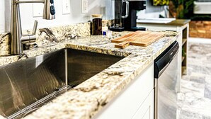 Una cocina moderna con encimera de granito, pileta de acero inoxidable y cafetera.
