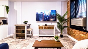 Una sala moderna con un televisor de pantalla plana montado en la pared, una pequeña mesa de madera, una planta en maceta y una pared de ladrillo decorativa.
