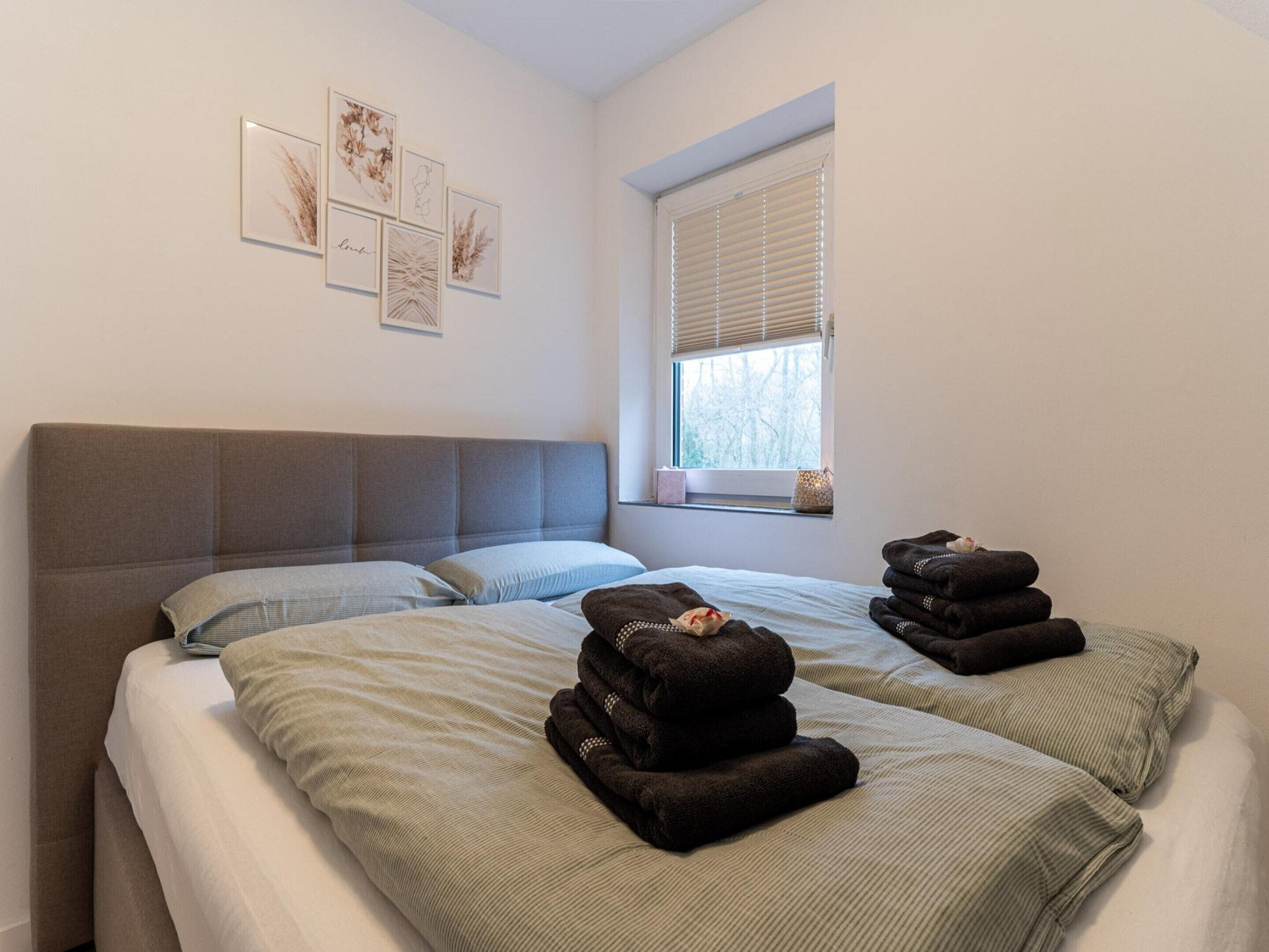 A bedroom with two beds, a window with blinds, and artwork on the wall.