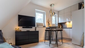A modern kitchen with a flat-screen TV, bar stools, and a dining area. - Ferienwohnung in St. Peter-ording (St. Peter-Ording)
