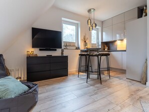 A modern kitchen with a flat-screen TV, bar stools, and a dining area.