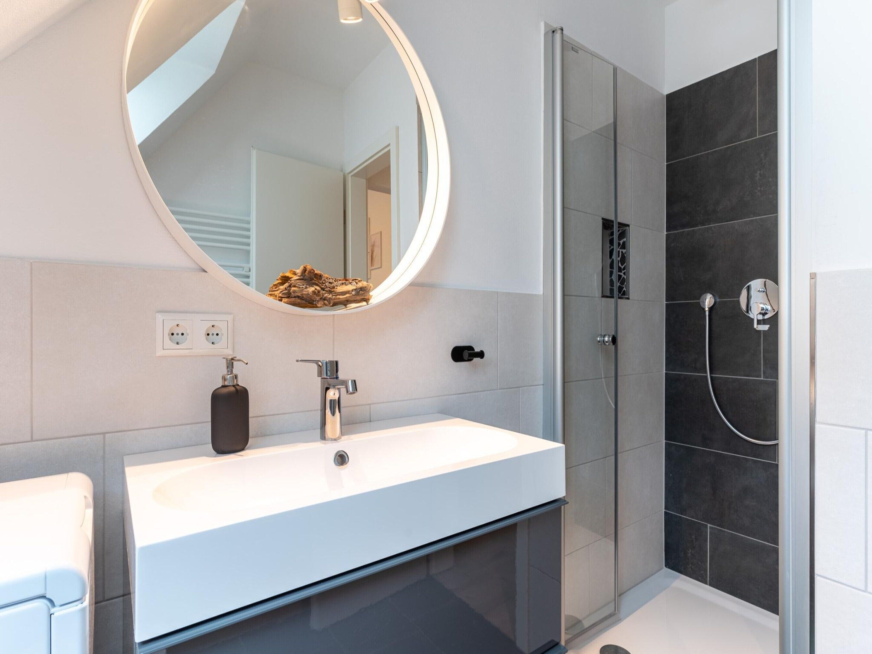 Een moderne badkamer met een witte wastafel, een ronde spiegel en een douche met glazen wanden.