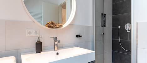 Een moderne badkamer met een witte wastafel, een ronde spiegel en een douche met glazen wanden.