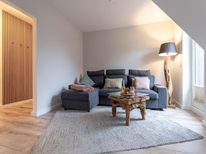 A modern living room with a sectional sofa, a glass coffee table, and a floor lamp. - Ferienwohnung in St. Peter-ording (St. Peter-Ording)