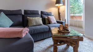 A modern living room with a dark-colored sofa, a glass coffee table, and a lamp. - Ferienwohnung in St. Peter-ording (St. Peter-Ording)