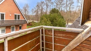 A residential area with a brick house, a wooden deck, and a view of trees and a green bush. - Ferienwohnung in St. Peter-ording (St. Peter-Ording)