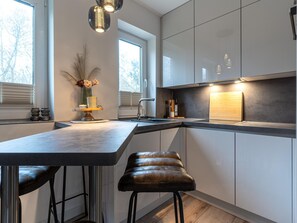 A modern kitchen with a central island, bar stools, and a view of the outdoors. - Ferienwohnung in St. Peter-ording (St. Peter-Ording)