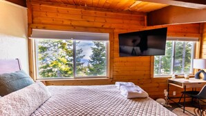A wooden cabin room with a bed, a desk, a TV, and large windows. - Mountain Serenity | Ski, Golf, Casino and Lake within 5 mile (Stateline)