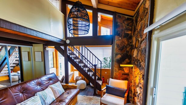 A spacious living area with a leather sofa, a staircase, and a stone wall. - Mountain Serenity | Ski, Golf, Casino and Lake within 5 mile (Stateline)