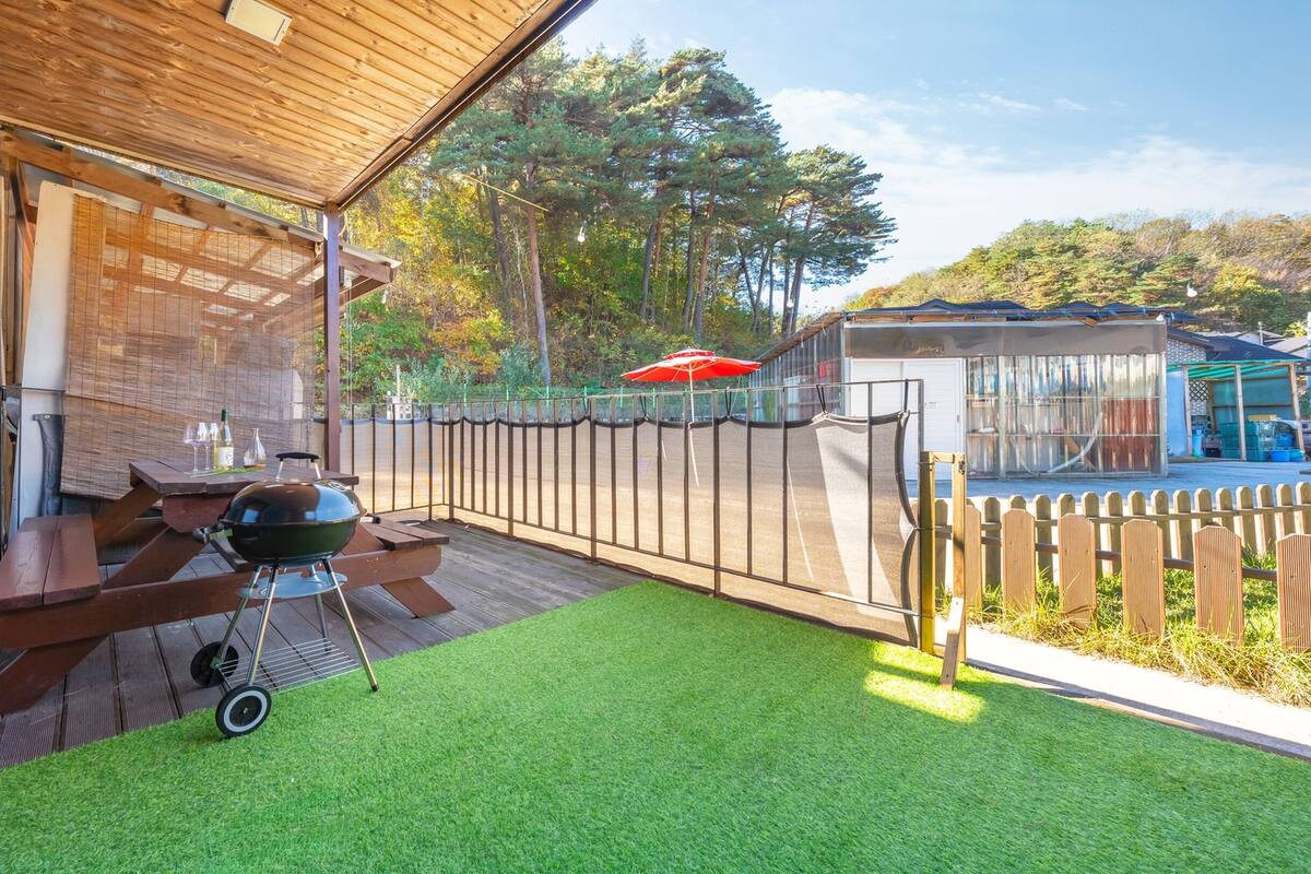 A patio with a barbecue grill, a wooden table, and a red umbrella.