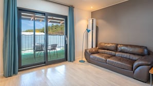 Een moderne woonkamer met een bruine leren bank, een staande lamp en een schuifdeur die leidt naar een terras buiten met stoelen en een tafel.