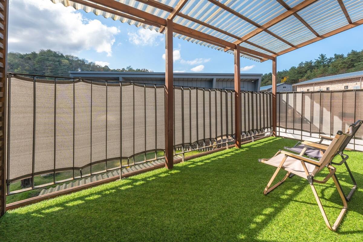 A covered patio with artificial grass, a seating area, and a view of a brick building.