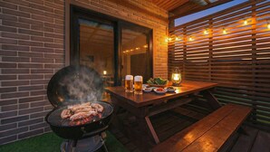 Een buitenbarbecue met een grill, twee bierglazen en een lantaarn op een houten tafel.