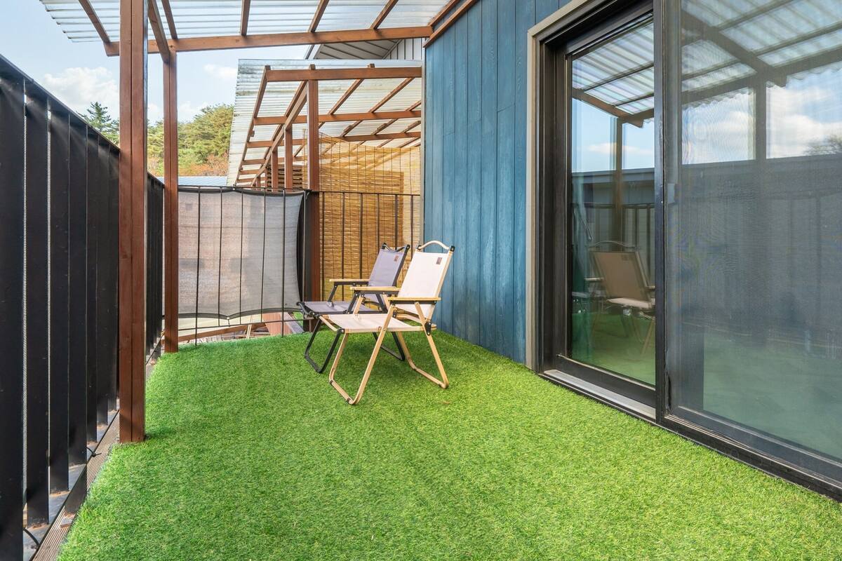 A patio with artificial grass, two folding chairs, and a glass door leading to a covered area.
