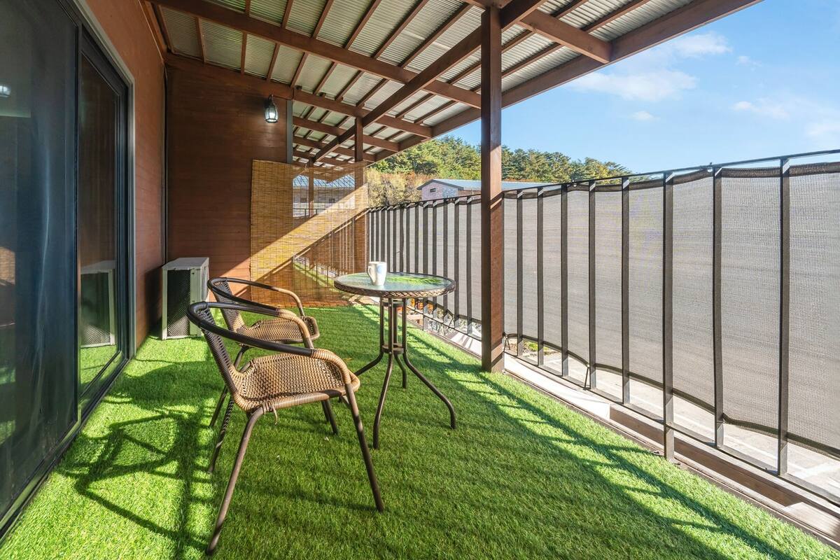 A balcony with artificial grass, a wicker chair, a small table, and a metal fence.