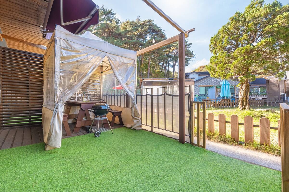A patio area with artificial grass, a barbecue grill, and a covered seating area.