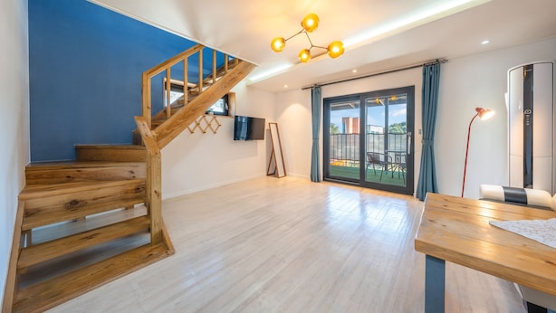 Een ruime kamer met een houten trap, een aan de muur bevestigde televisie, een balkon met uitzicht en een moderne lamp.