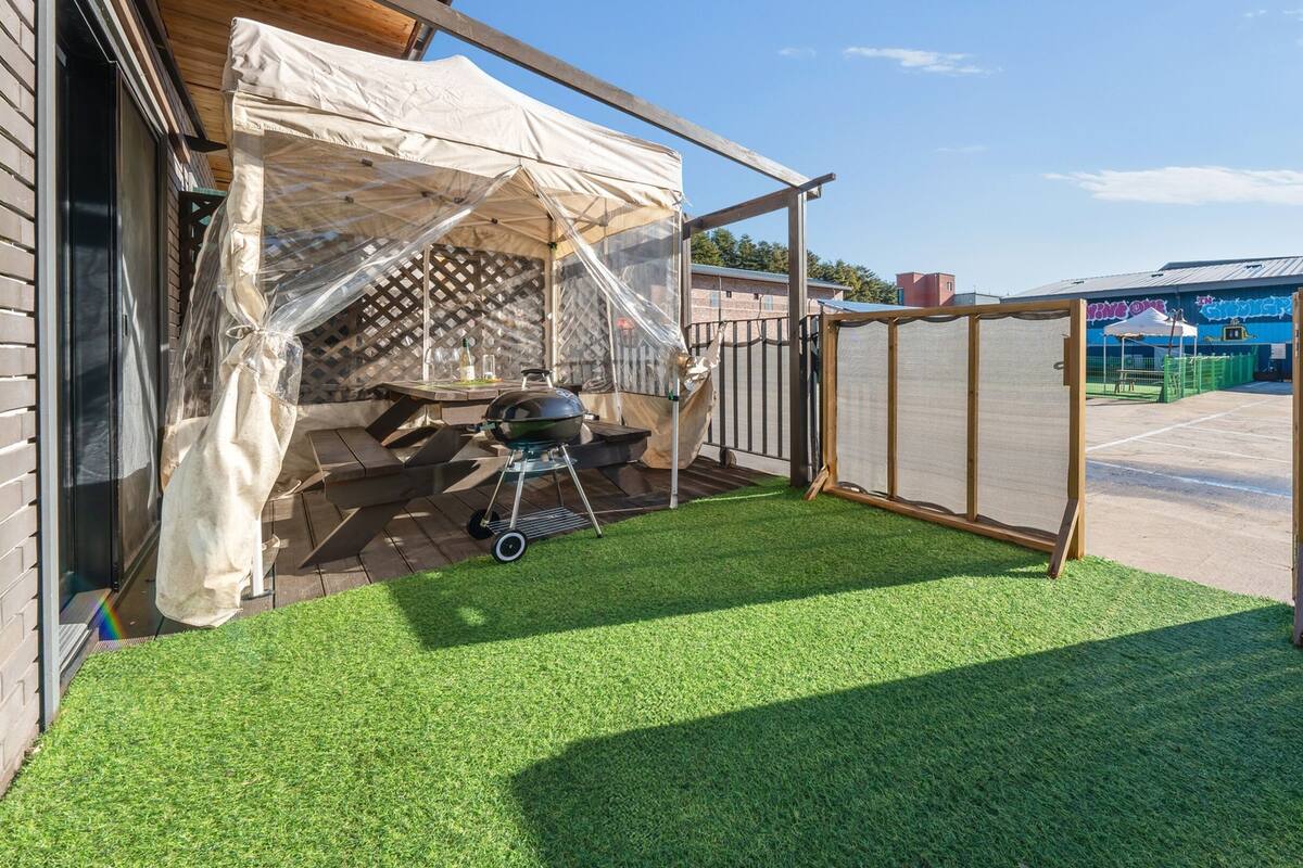 A patio with artificial grass, a barbecue grill, and a tent structure.