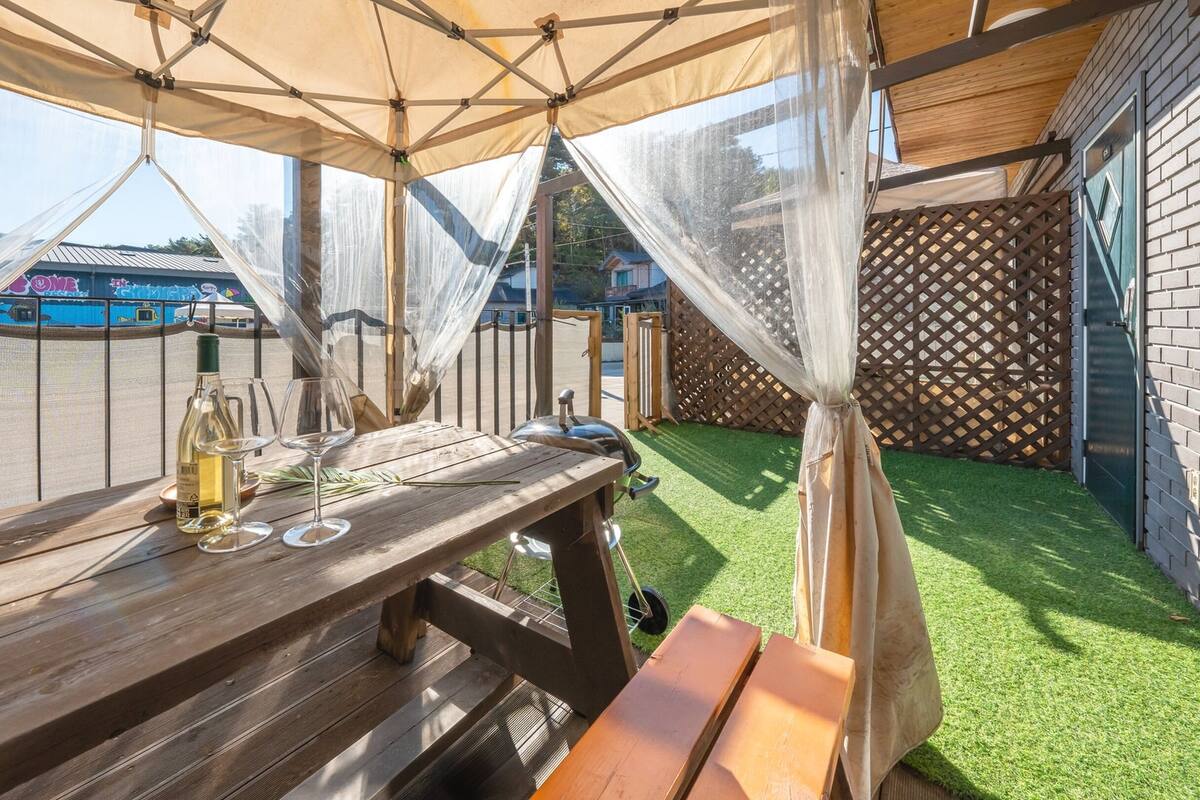 A wooden table with a bottle of wine and glasses, under a tent with sheer curtains.