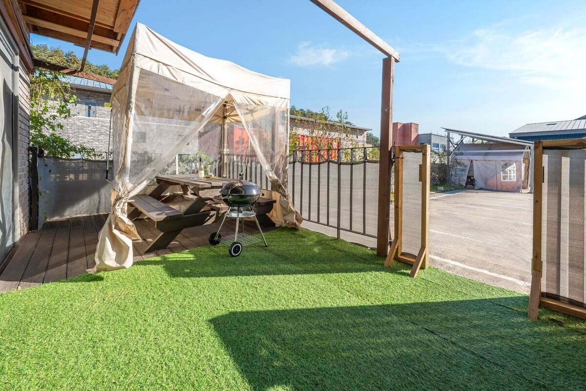 A backyard with artificial grass, a barbecue grill, and a covered seating area.