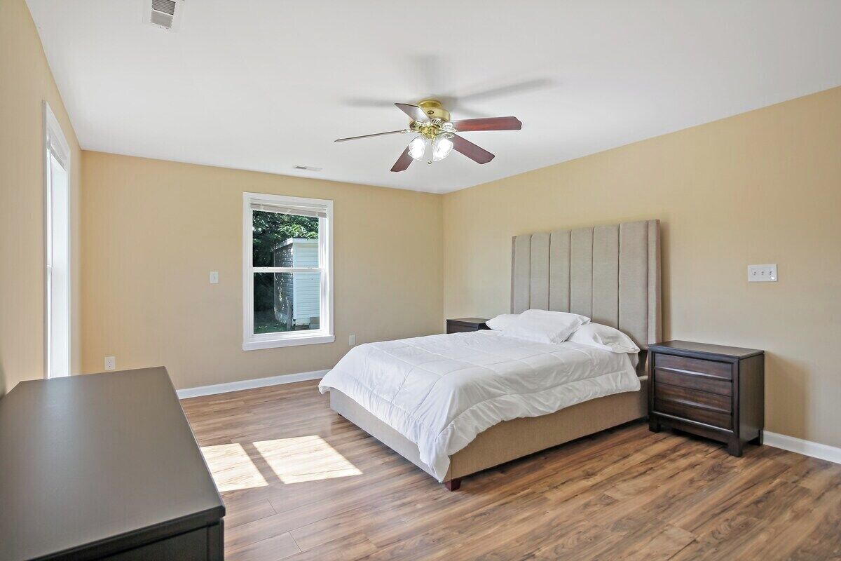 Un dormitorio con cama, mesita de noche, cómoda, ventilador de techo y ventana.