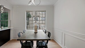 Ein Essbereich mit einem rechteckigen Tisch, sechs Stühlen, einer Vase und einem Fenster mit Blick auf Gebäude.