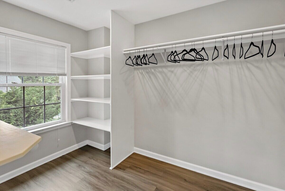 Une pièce avec une fenêtre, des étagères blanches et une tringle à rideaux avec des crochets.