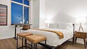 A hotel room with a bed, two chairs, a desk, a lamp, and a window with blinds. - Tysons 1BR + Queen Den | Rooftop Pool & Balcony (Tysons)