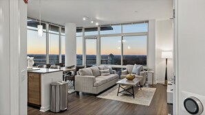 A spacious living room with a large window, a sofa, a coffee table, and a dining area with chairs and a table. - Tysons 1BR + Queen Den | Rooftop Pool & Balcony (Tysons)