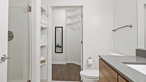 A modern bathroom with a shower, toilet, and a walk-in closet with a hanging rack. - Tysons 1BR + Queen Den | Rooftop Pool & Balcony (Tysons)