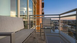 A balcony with a view of a cityscape at dusk, featuring a modern building with glass and brick elements. - Tysons 1BR + Queen Den | Rooftop Pool & Balcony (Tysons)