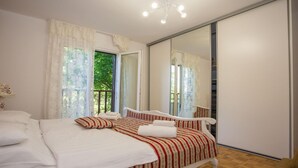 A bedroom with a bed, a large mirror, and a view of greenery outside. - Beautiful Apartment in Prime Location (Porec)